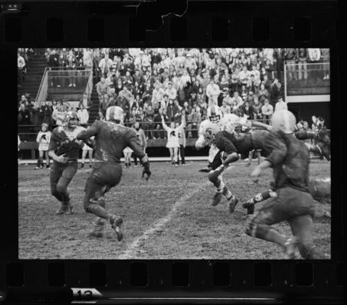 Muddy football players in action on Seagram Field in front of a large crowd in the stands.