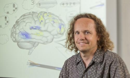 Photo of Professor Eliasmith seated in front of a graphic of the human brain