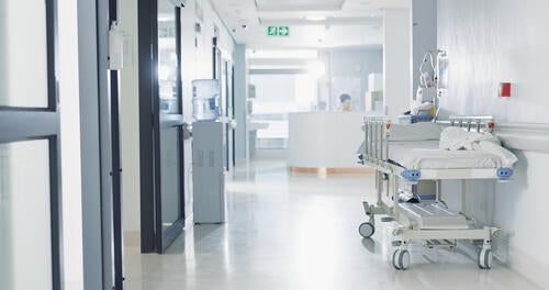 Hospital hallway with a bed along the wall and a nurses' station in the distance