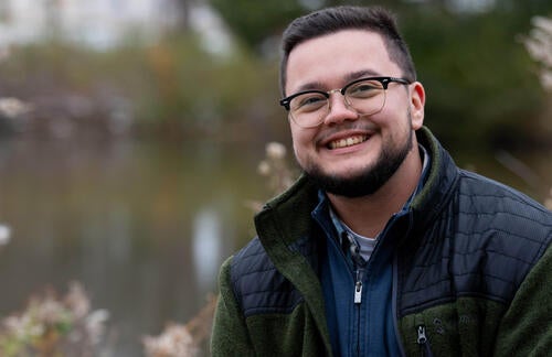 Kian Drew smiles at camera while posing in front of estuary