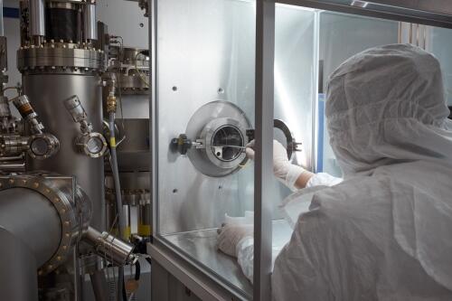 Researcher in gloves and protective clothing working with long instrument in Molecular Beam Epitaxy lab.