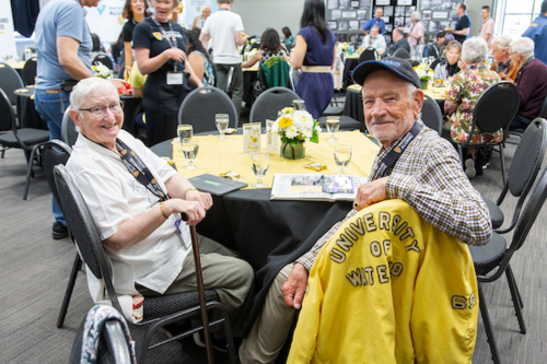 Two alum sitting at a table, turning and smiling at the camera