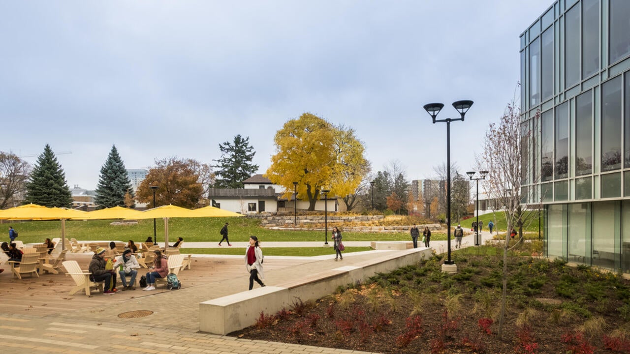 Students sitting at tables talking and other students walking on a path