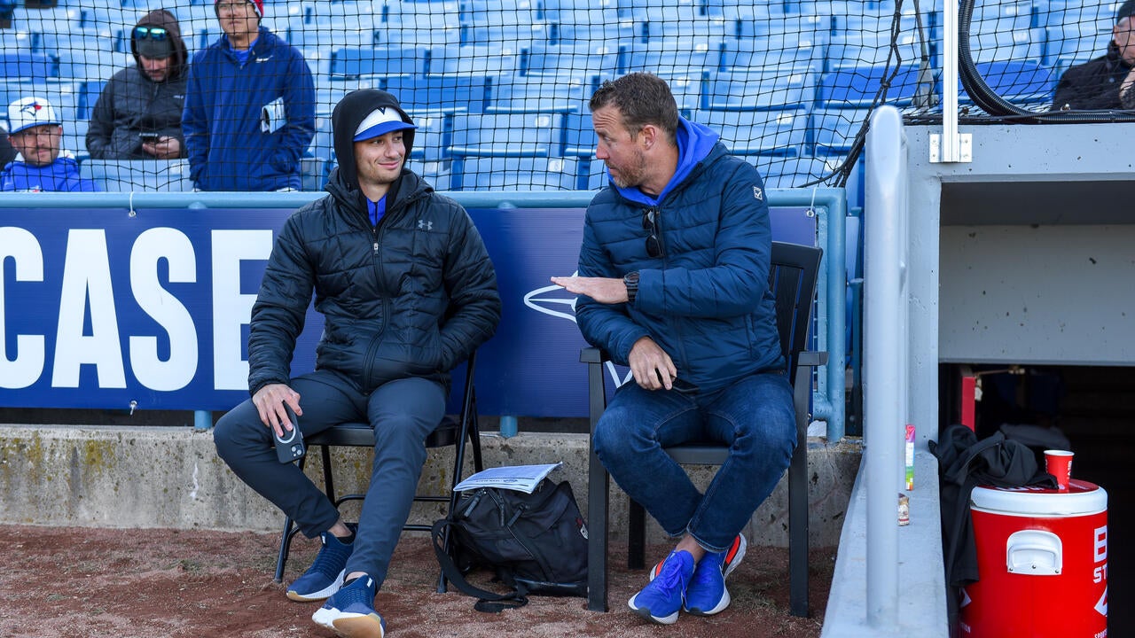 Jesse Levine chats with TJ Burton while seated beside a baseball dugout.