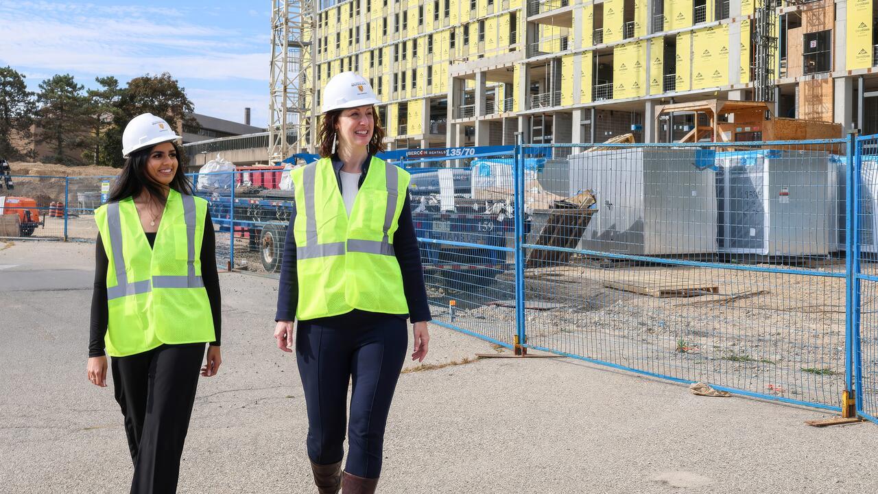 Leia Minaker and a student walk near a construction site while wearing safety equipment including hard hats