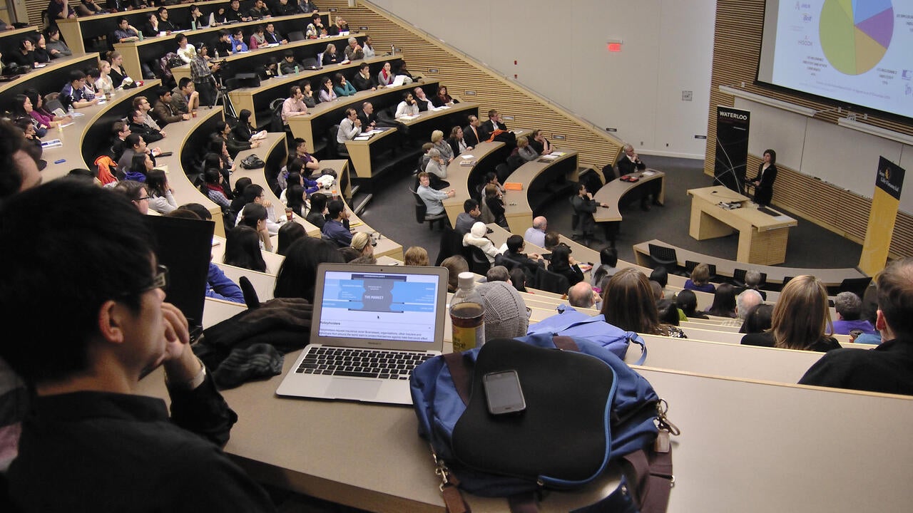 Theatre classroom with students using laptops and a professor lecturing at the front