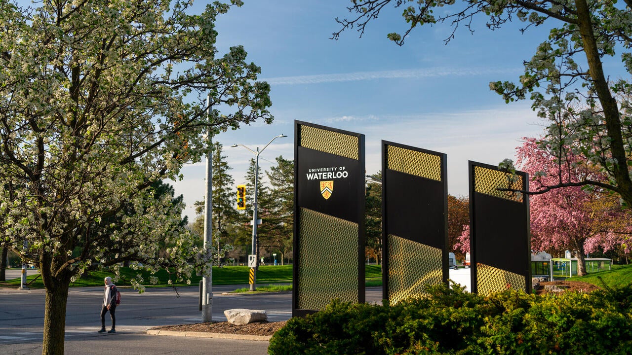 University of Waterloo signage on University Avenue at sunset with a person below the tree walking to cross the street