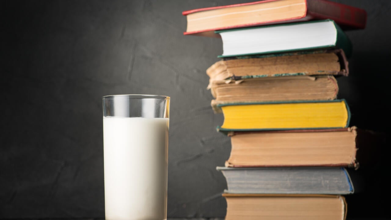 glass of milk stands next to pile of old books