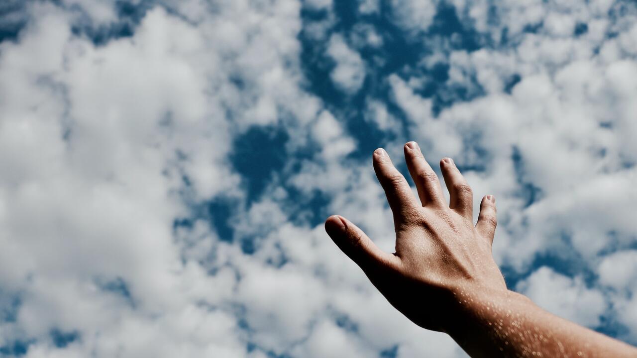 Hand raising up to a blue, cloudy sky