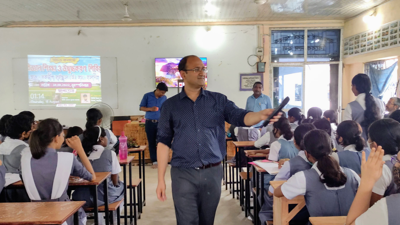 Dr. Rajibul Islam holding a mic addresses students seated at desks in a classroom with a projected presentation at the front.
