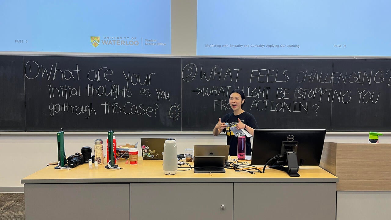 Student in front of a chalkboard smiling with thumbs up