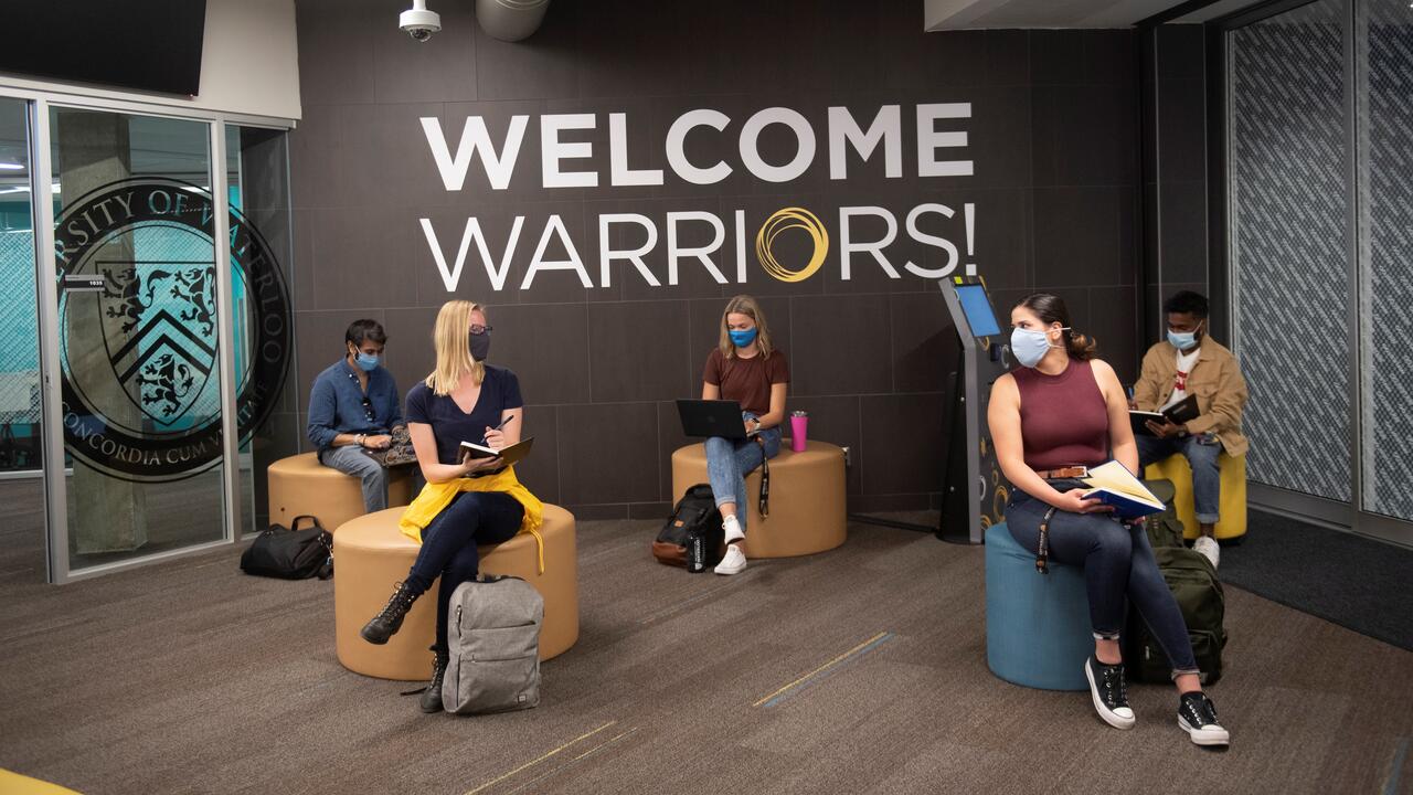 students sit inside a campus building, socially distanced with masks on