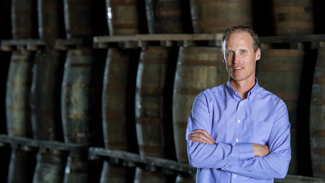 Don Livermore stands, arms crossed, in front of a row of whisky barrels