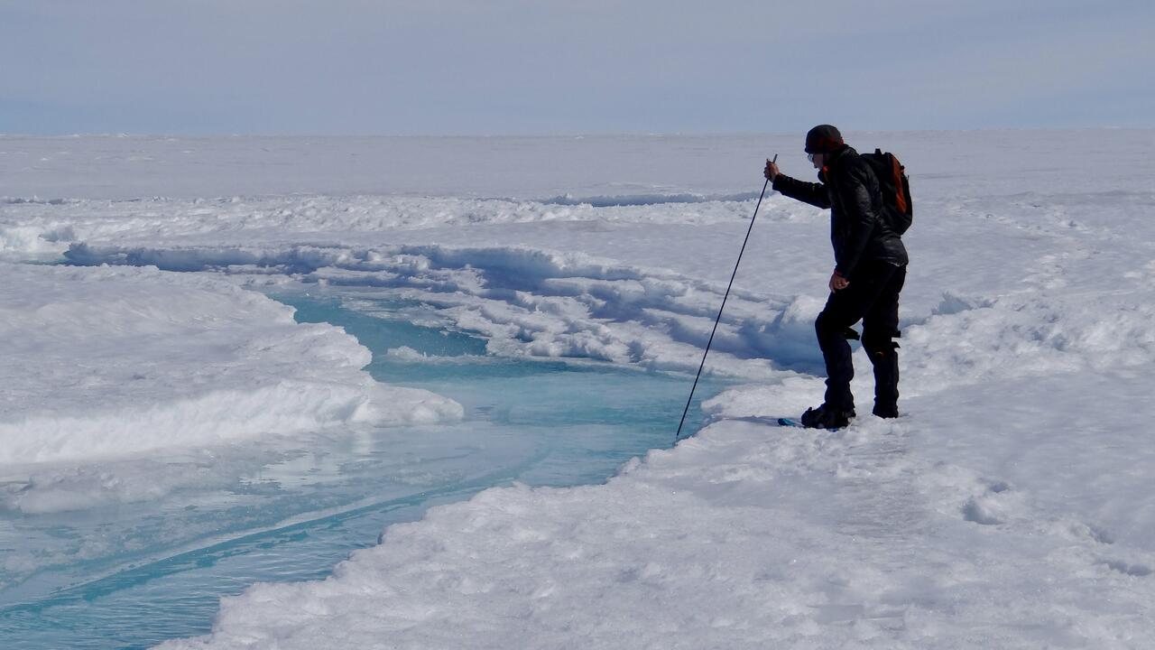 Man inserts measuring stick into a stream on top of ice