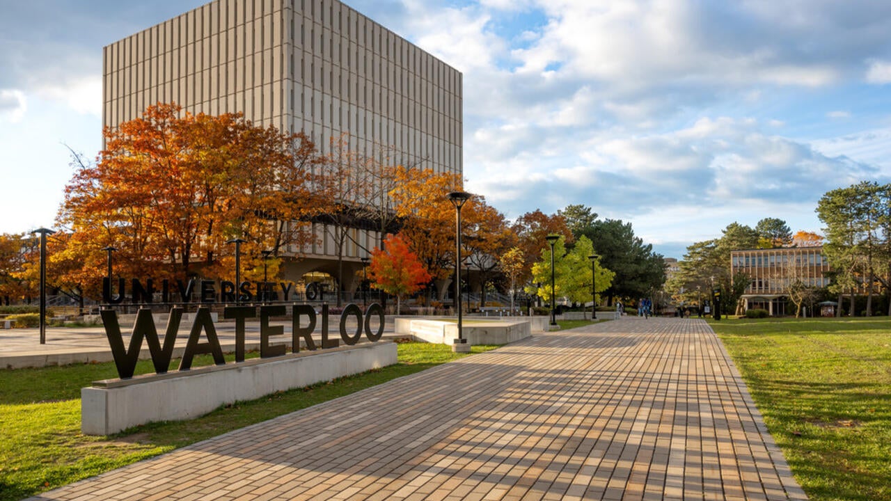 Wide shot of Dana Porter Library in the Fall along with the University of Waterloo sign