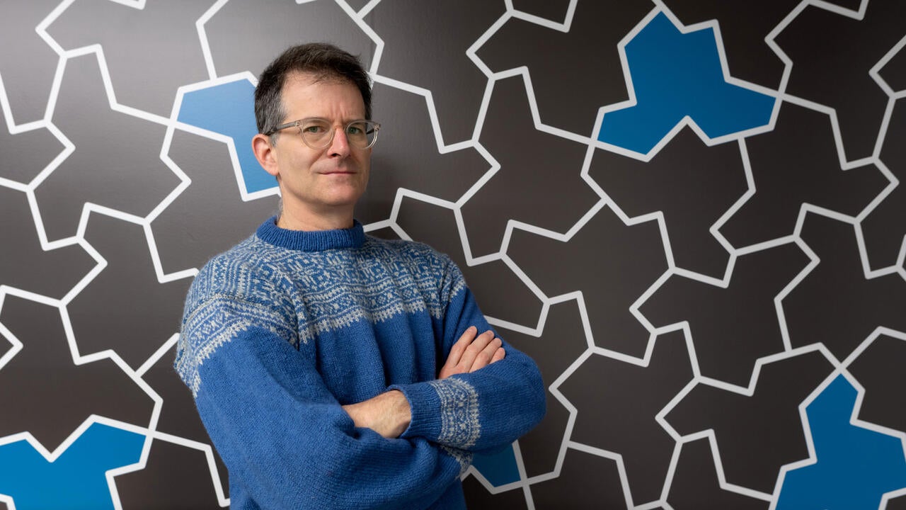 Professor Craig S. Kaplan stands in front of a wall of hat-shaped einstein tiles 
