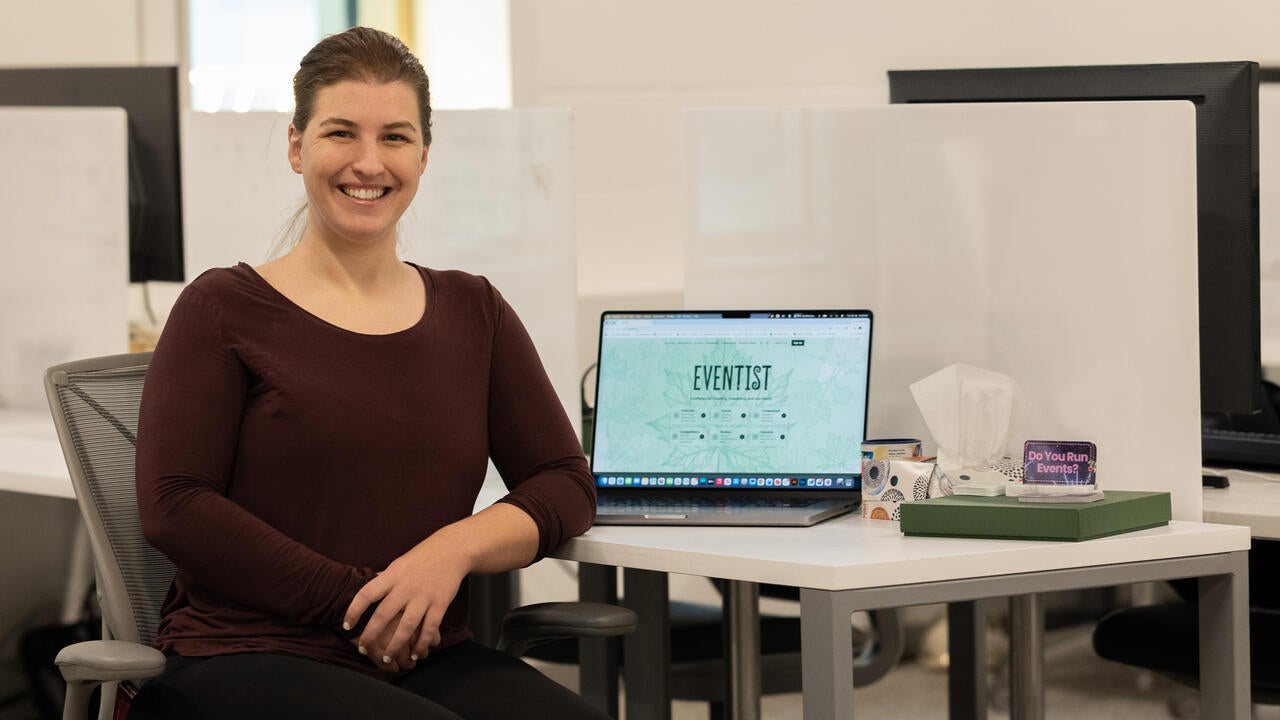 Ciara Azam sitting by a desk with a laptop showing the Eventist landing page next to a box of tissues and trinkets