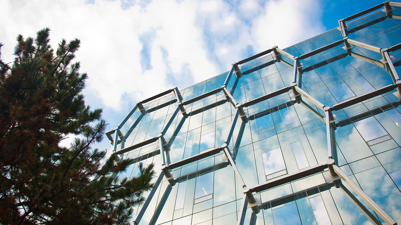 Low angle of the IQC building exterior featuring a tree and clouds reflecting in the building's windows.