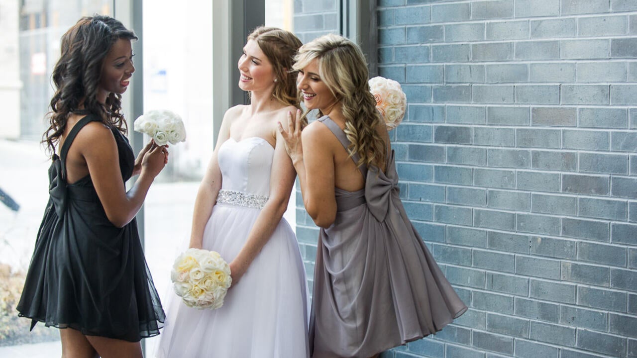 Bride holding white flowers and two bridesmaids smiling with her