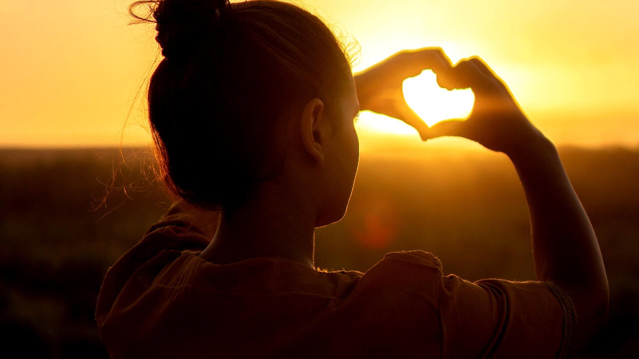 Young woman making a heart with her hands in front of the sun