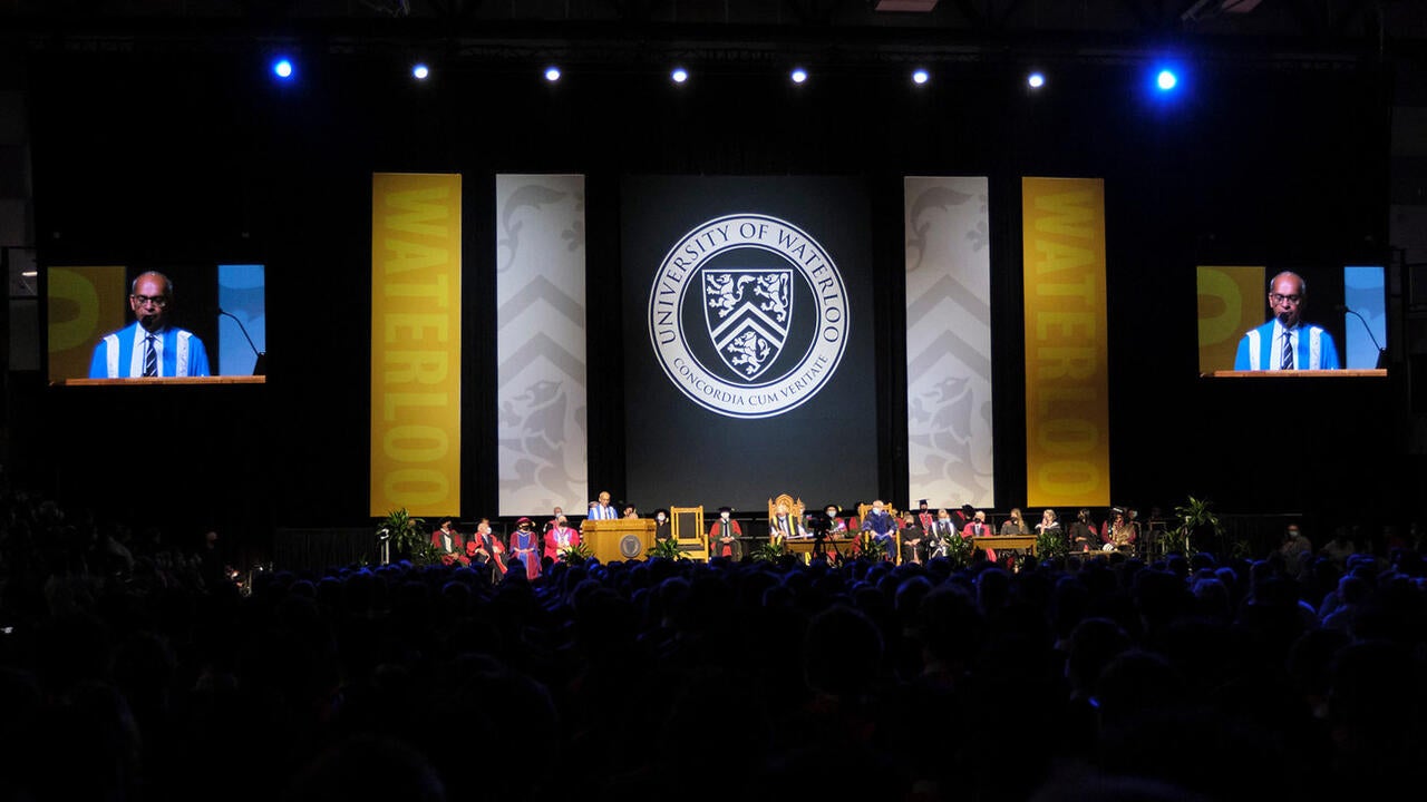 Convocation stage features Vivek Goel at podium and dignitaries seated with the Waterloo crest on a banner behind the stage.