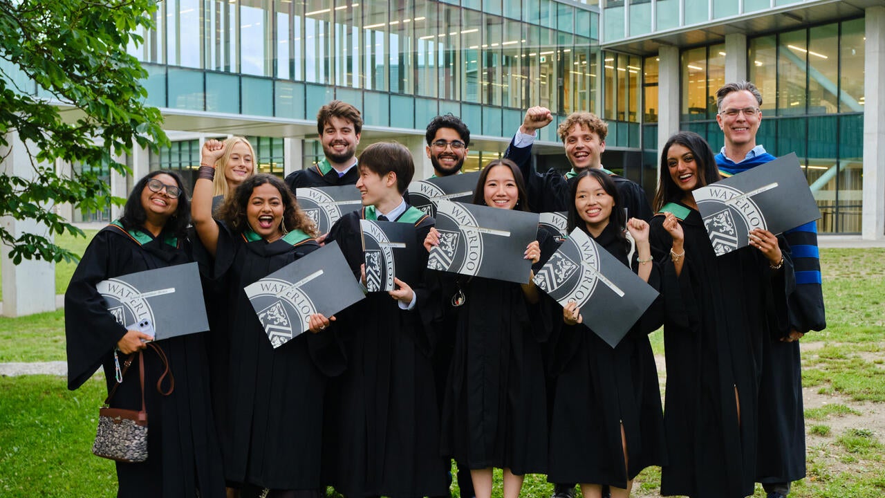 Groyp of SFM gradates in their conovcation robes holding diplomas and celebrating 