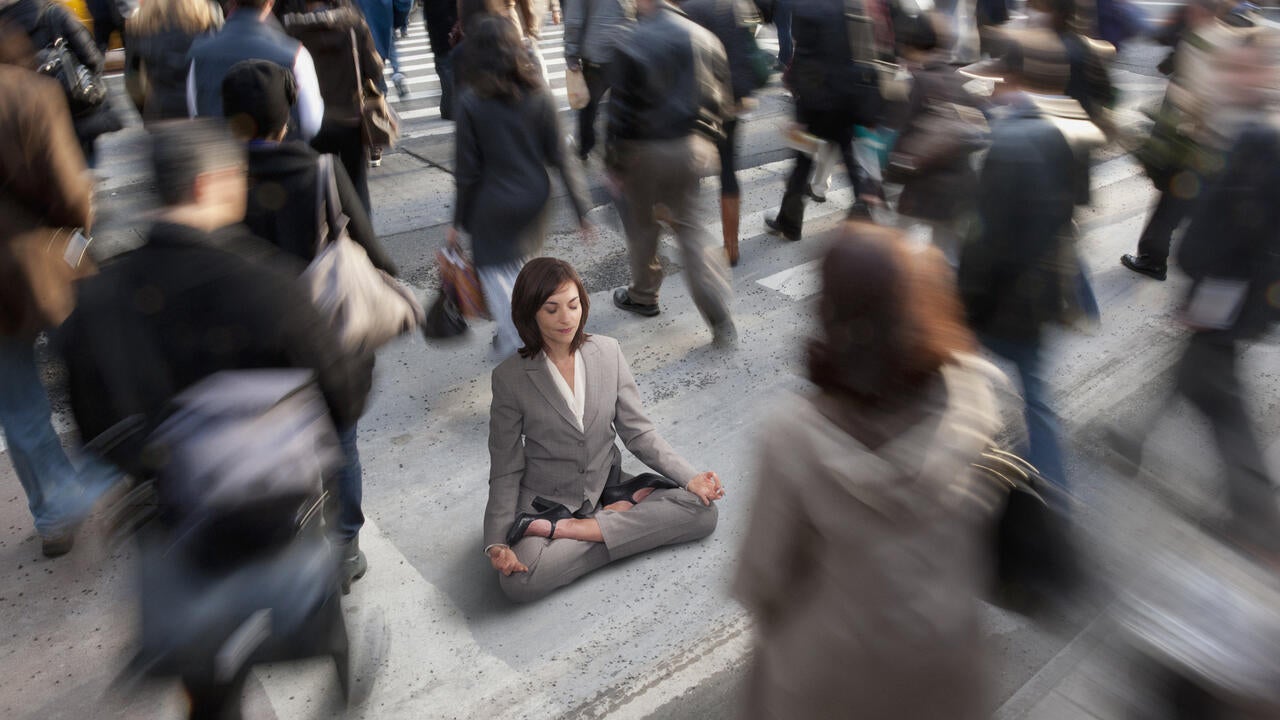 Woman dressed in business suite practicing yoga in busy urban crosswalk