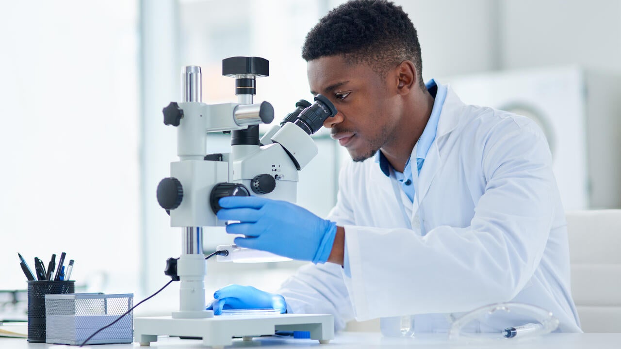 A focused young male scientist looking at test samples through a microscope inside of a laboratory 