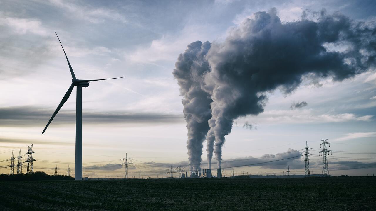 单风力涡轮机，一个燃煤发电厂，背景是污染和电力塔。