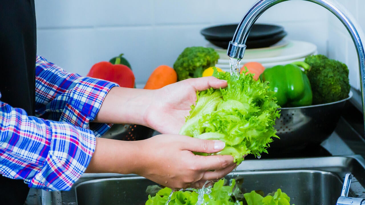 A person washing lettuce under running water.