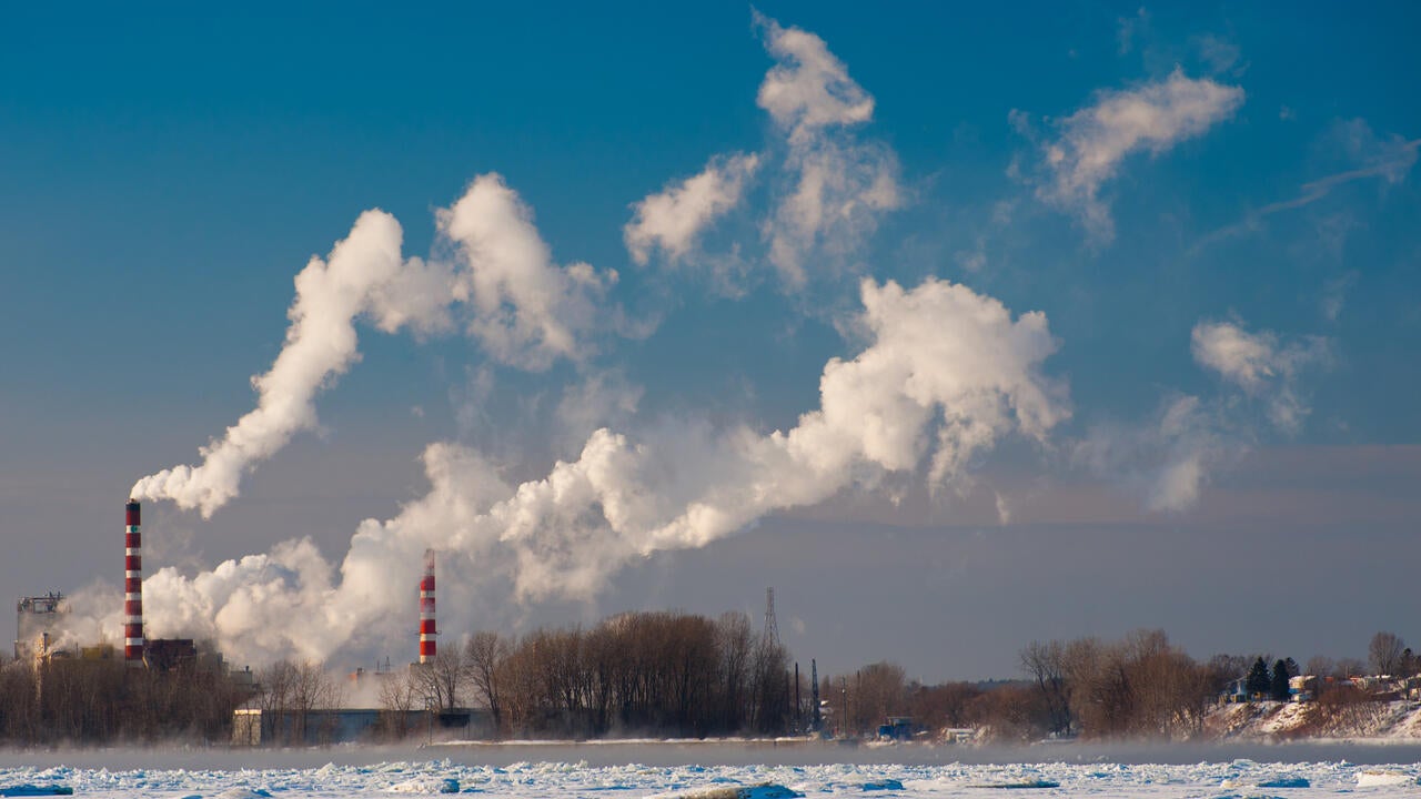 aper mill with its smokestacks spewing smoke against blue sky as across St-Lawrence River, Trois-Rivieres, Quebec, Canada.