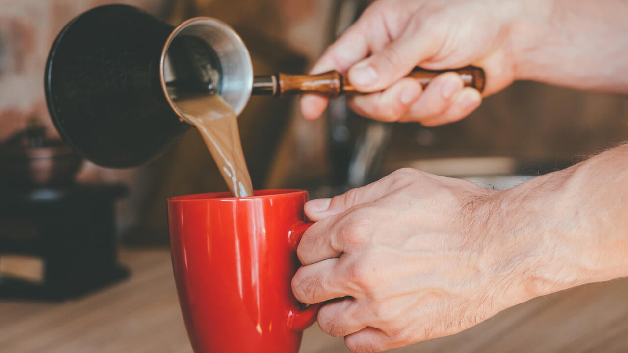 Man with jezve pouring latte into red mug.