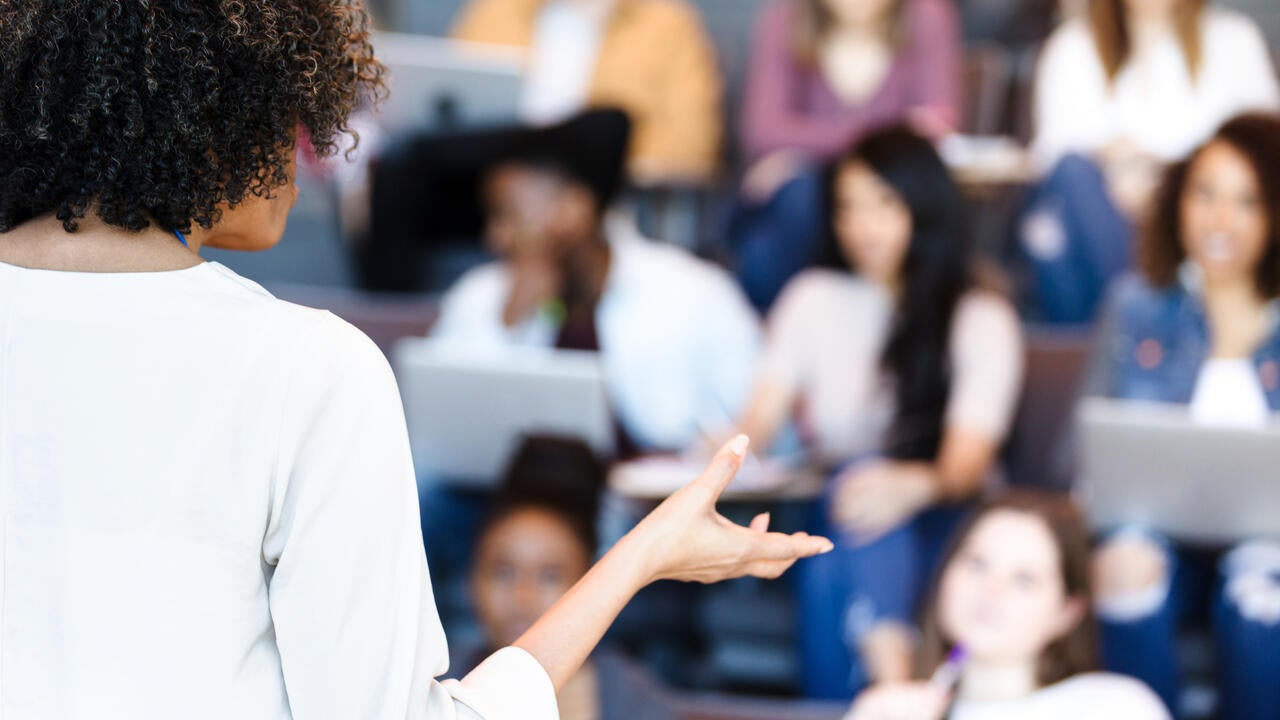 Unrecognizable female professor gestures while teaching diverse college students