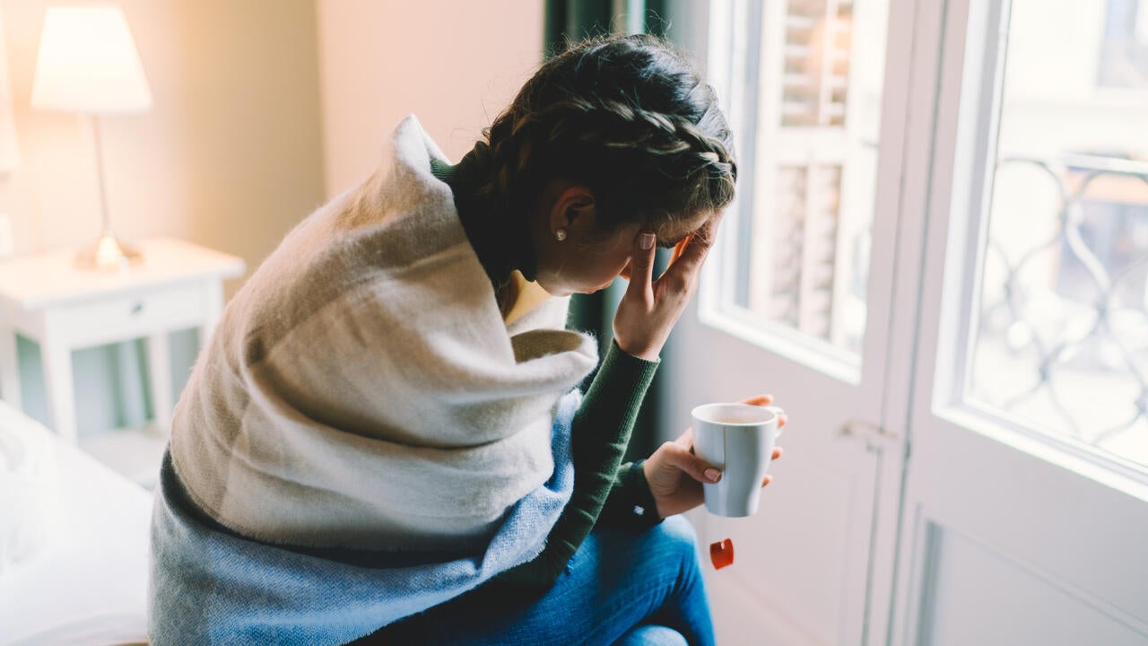 Woman with temperature staying home wrapped in scarf and drinking hot tea