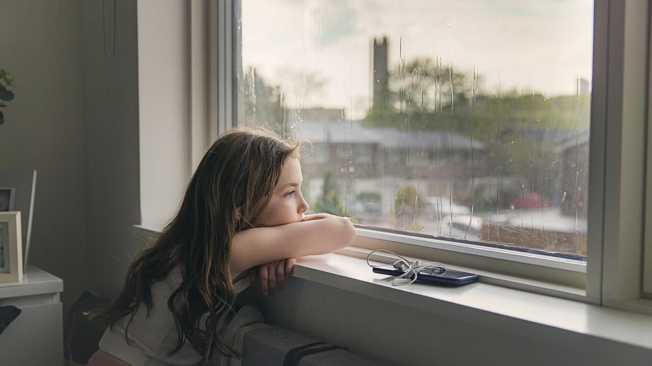 Young girl looking out of window on a rainy day 