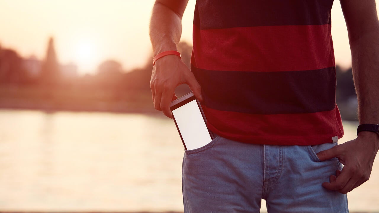 Man holding cellphone in pocket near river.