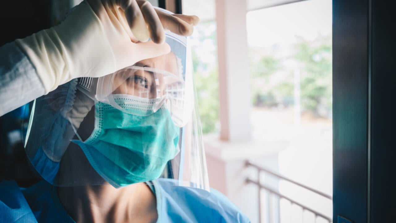 A nurse wearing a face mask looks through a window 