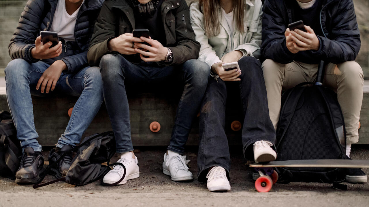 Teenagers sit on their cell phones at the park