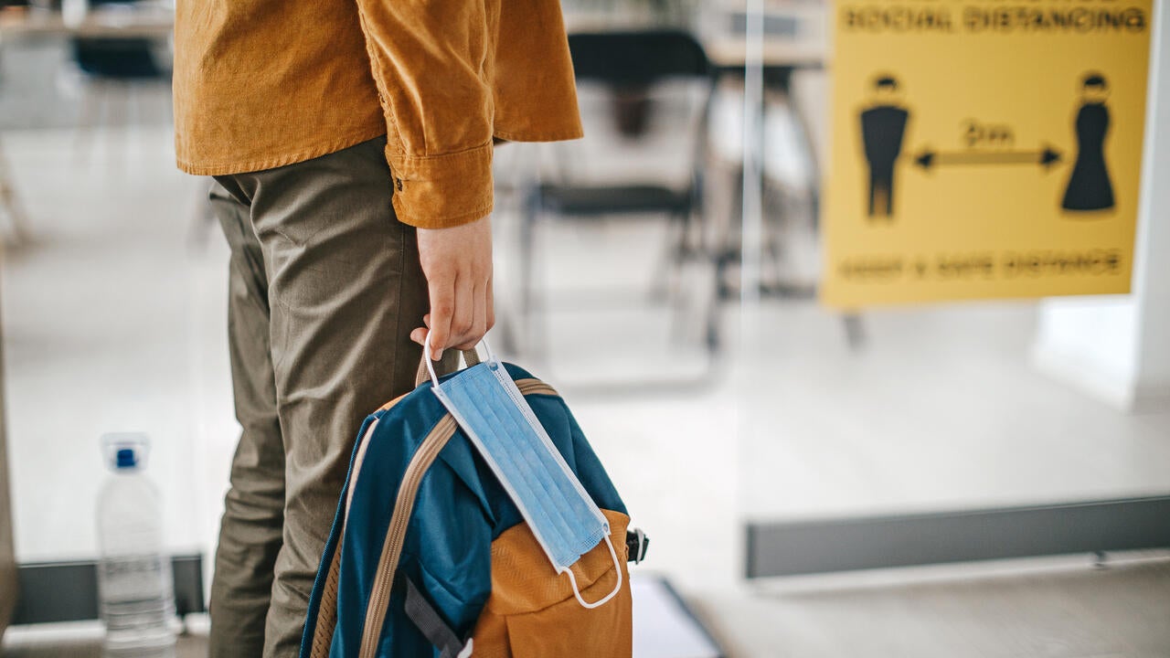 A person holding a knapsack bag and a face mask