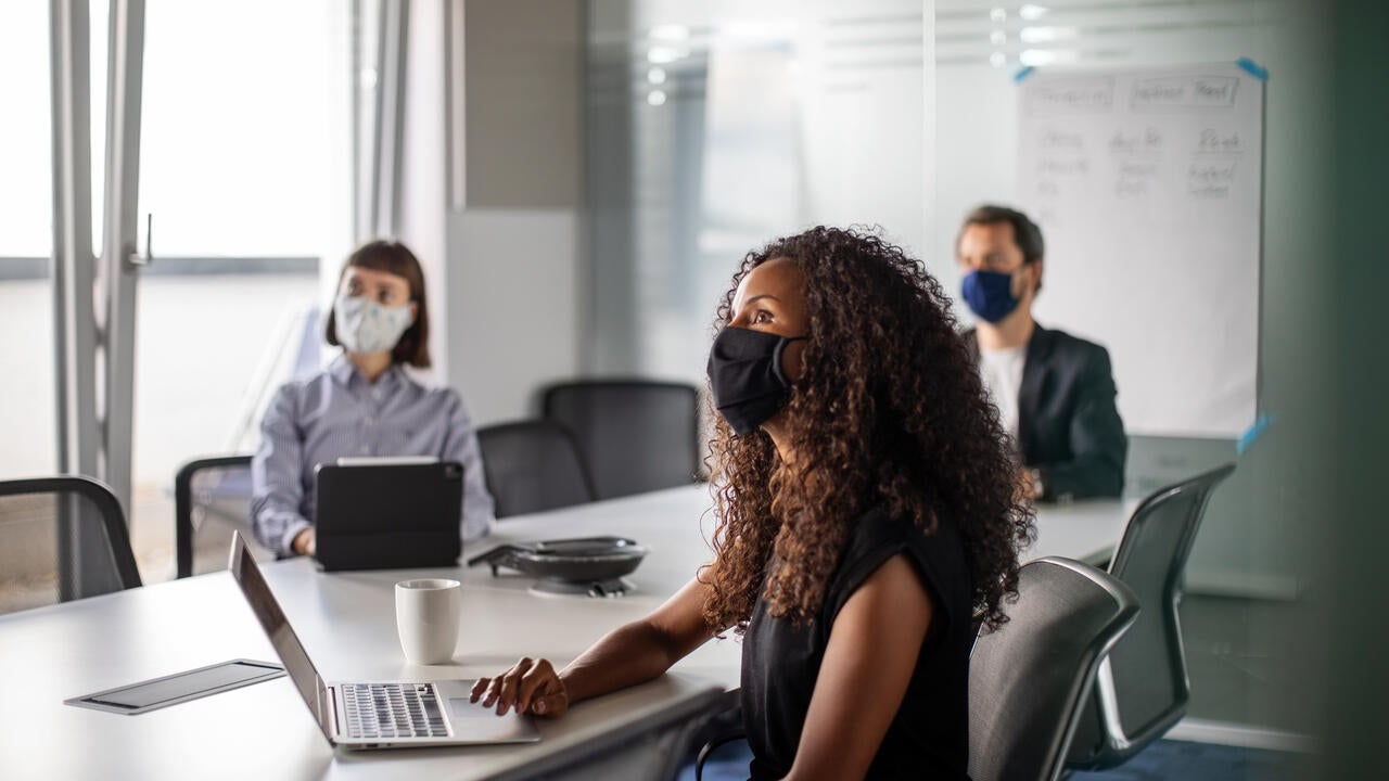 Team of business professionals wearing face mask sitting in office boardroom during a meeting.