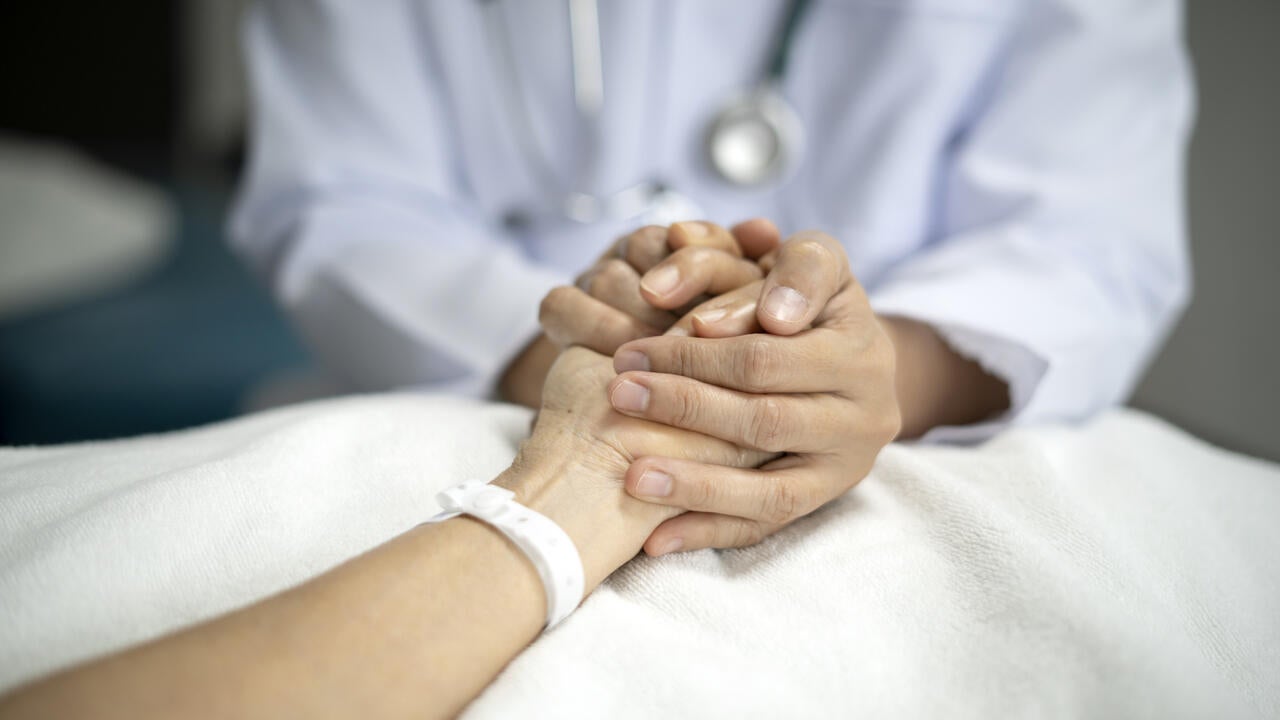 Doctor holding hand of senior female patient to give her support on her hospital bed 