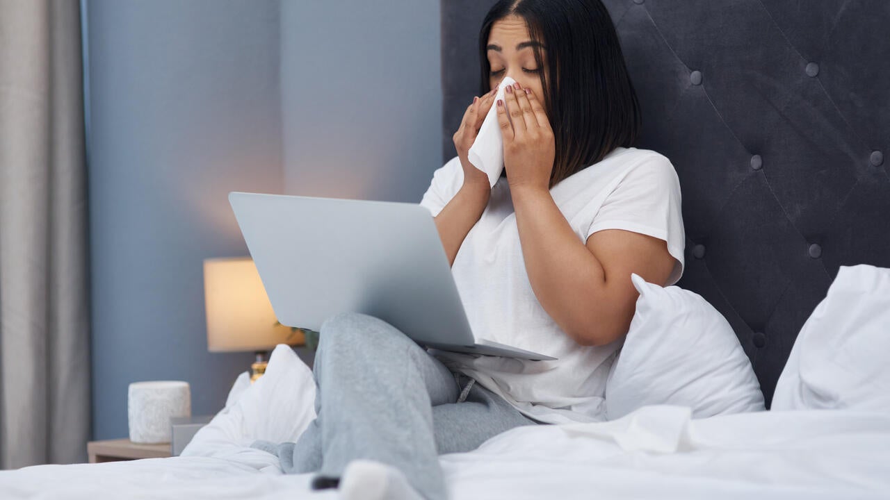 A woman sick in bed at home with a laptop 