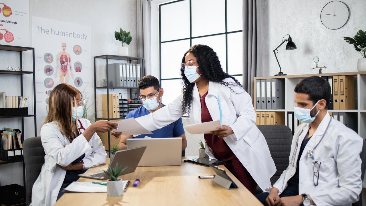 Doctors in protective masks with gadgets co-working at office