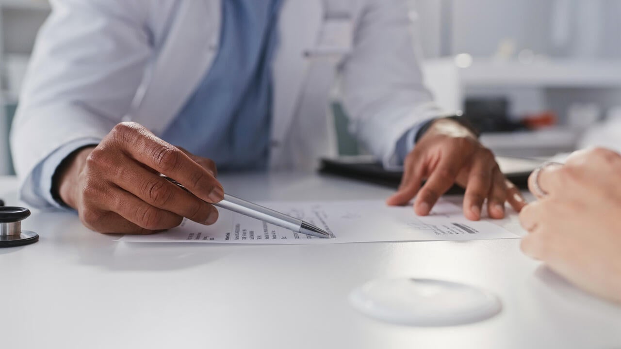 Cropped shot of an unrecognizable doctor sitting and reading test results with his patient during a consultation in his clinic 