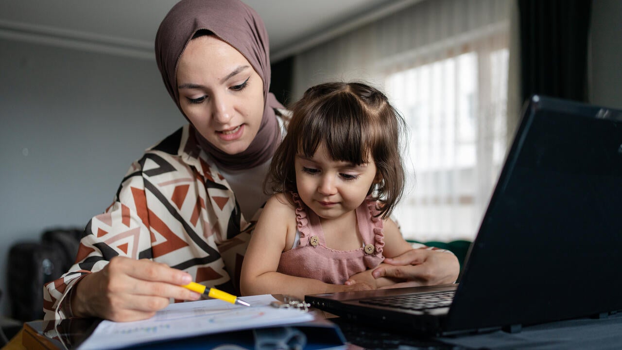 Photo of a mother studying while her child is in her lap. 