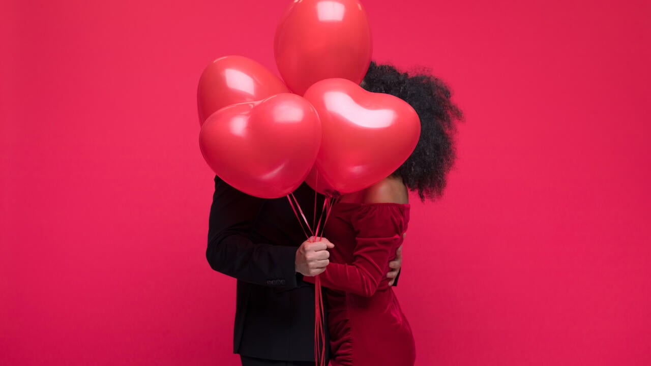 Young couple wearing elegant covering with bunch of heart shaped balloons.
