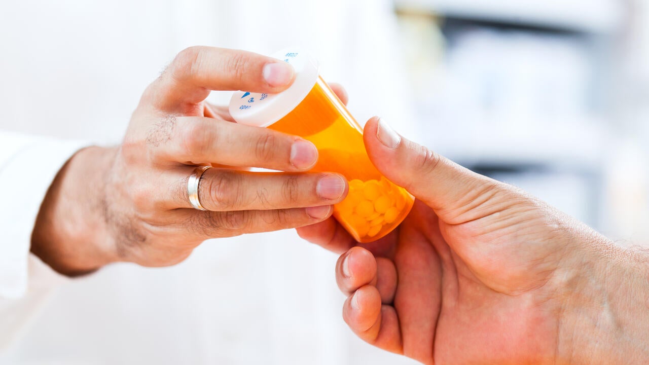 Close-up shot of doctor’s hand giving a bottle of pills to senior patient.