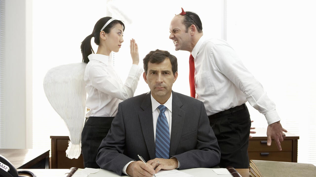 Executives with halo and devil horns standing behind businessman 