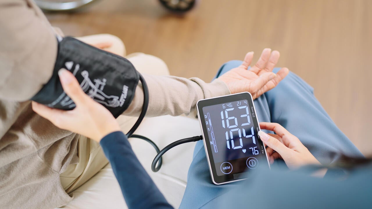 A nurse checks the blood pressure and heart rate of a woman as both sit on a bed.
