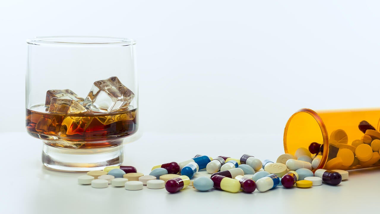Whiskey glass, with ice cubes, beside a large amount of drugs, capsules and pills